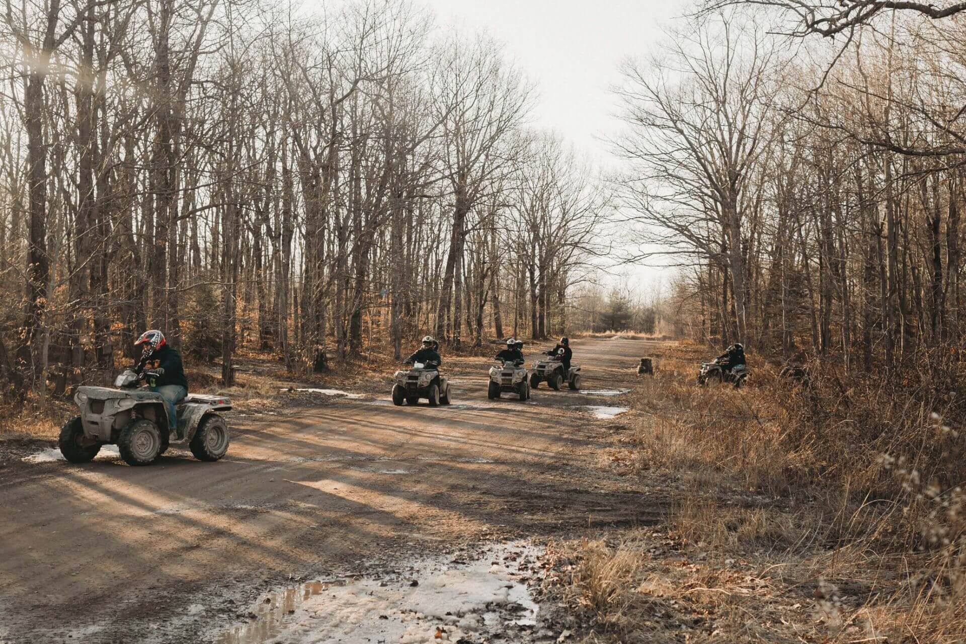A group of people are riding atvs down a dirt road in the woods.