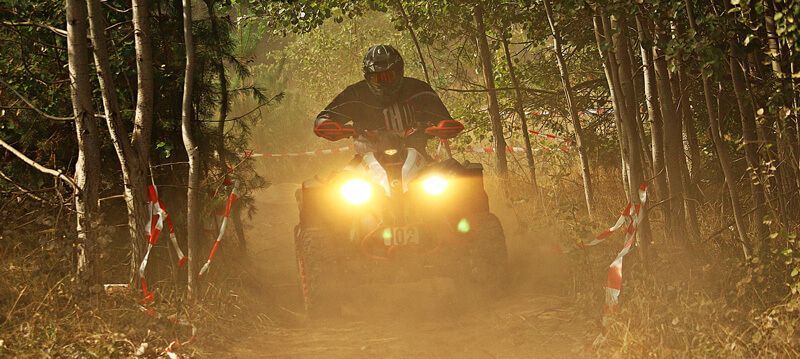 A man is riding an atv on a dirt road in the woods.