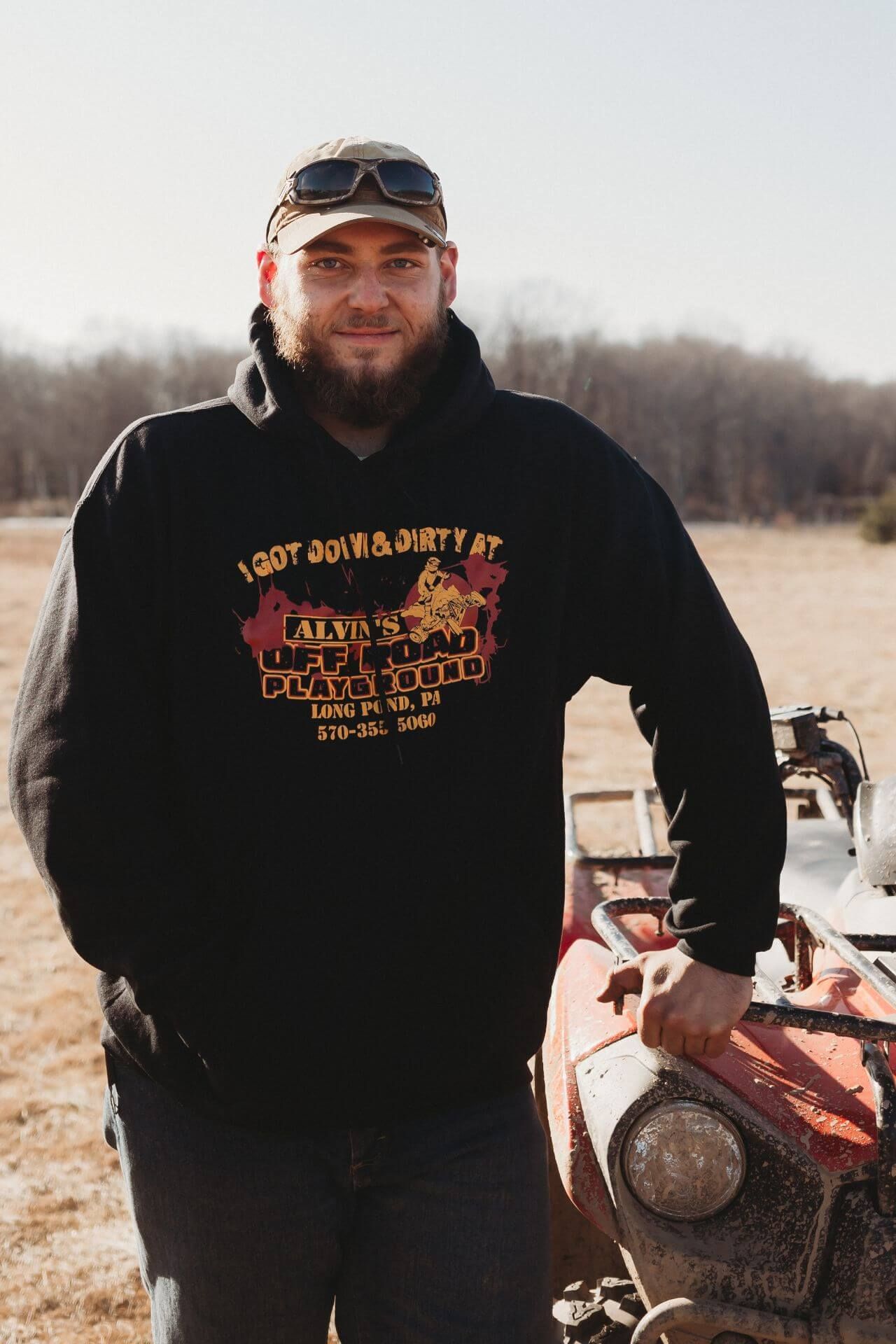A man in a black hoodie is standing next to a red atv.