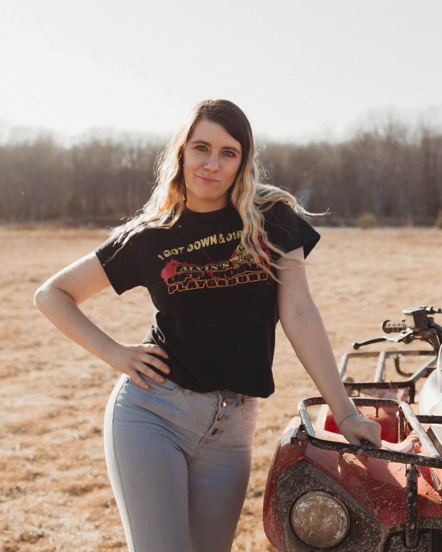 A woman is standing next to a red atv in a field.
