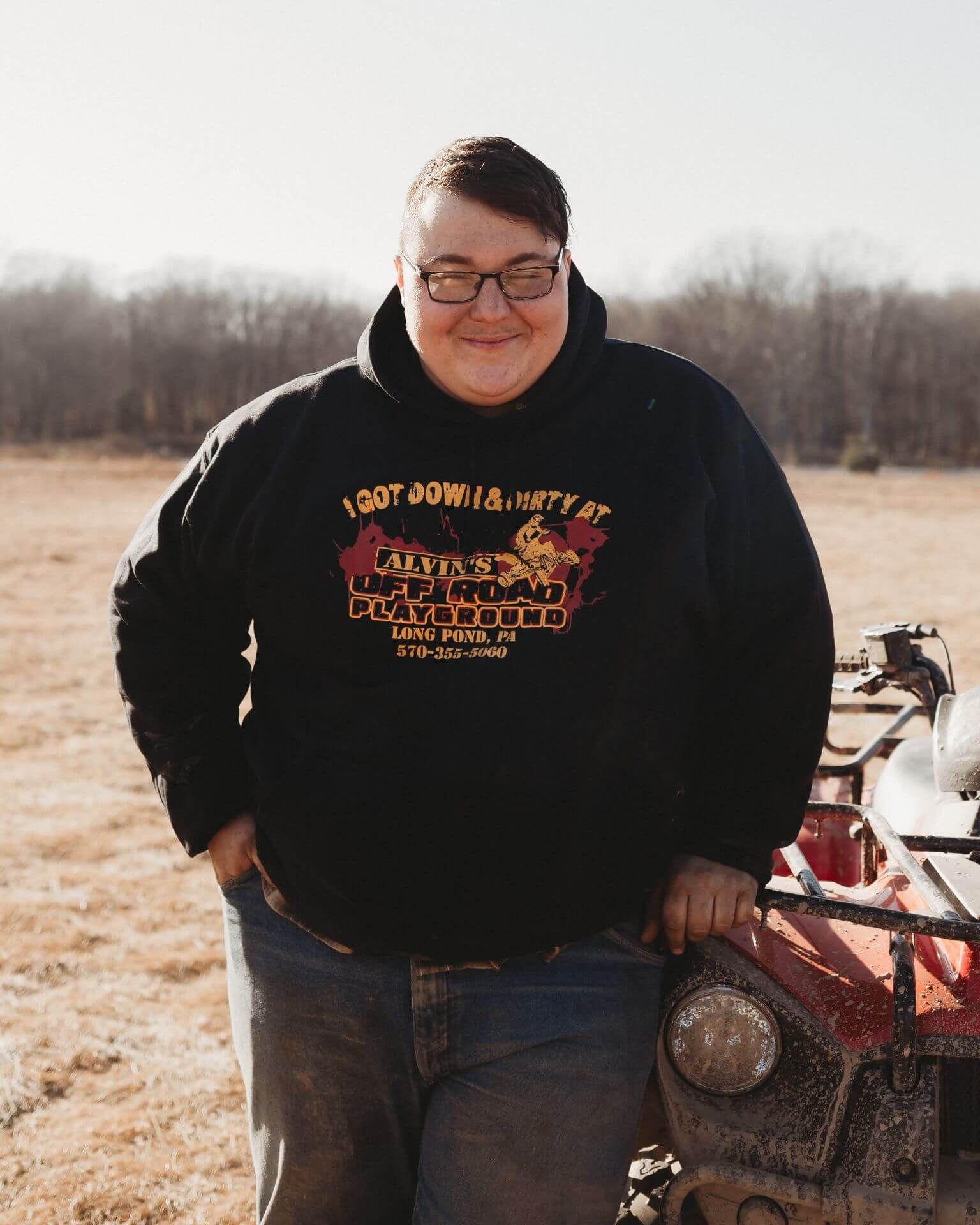 A man in a black hoodie is standing next to a red atv.