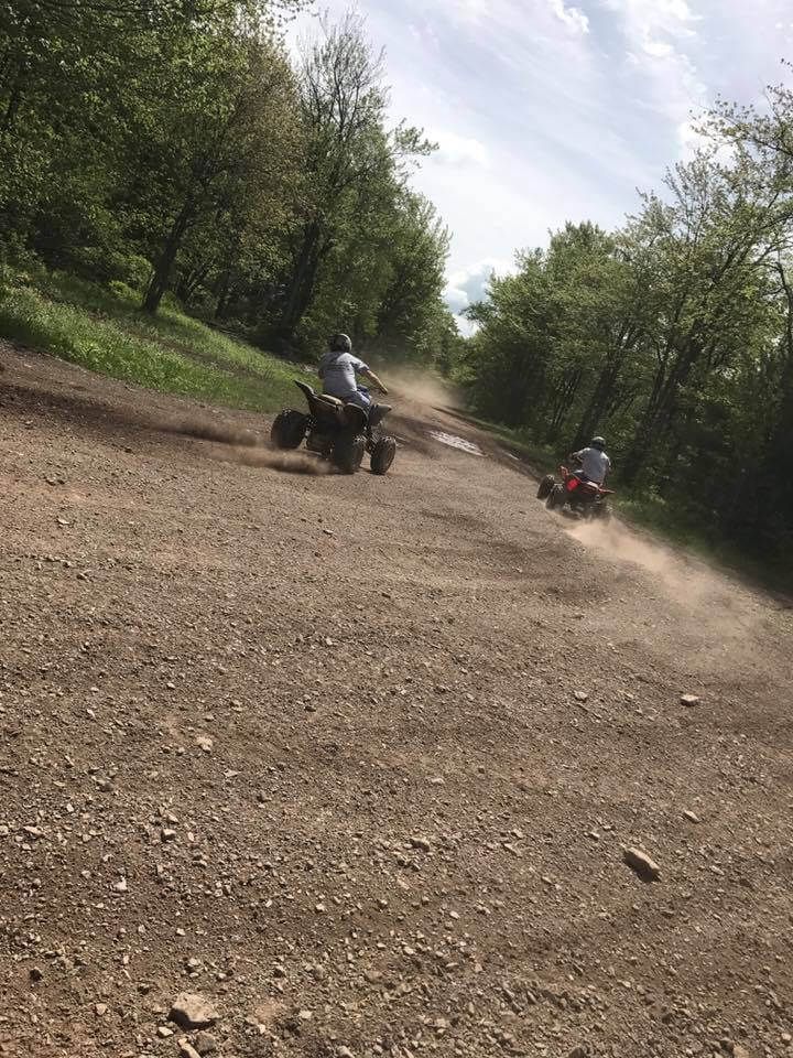Two people are riding atvs down a dirt road.