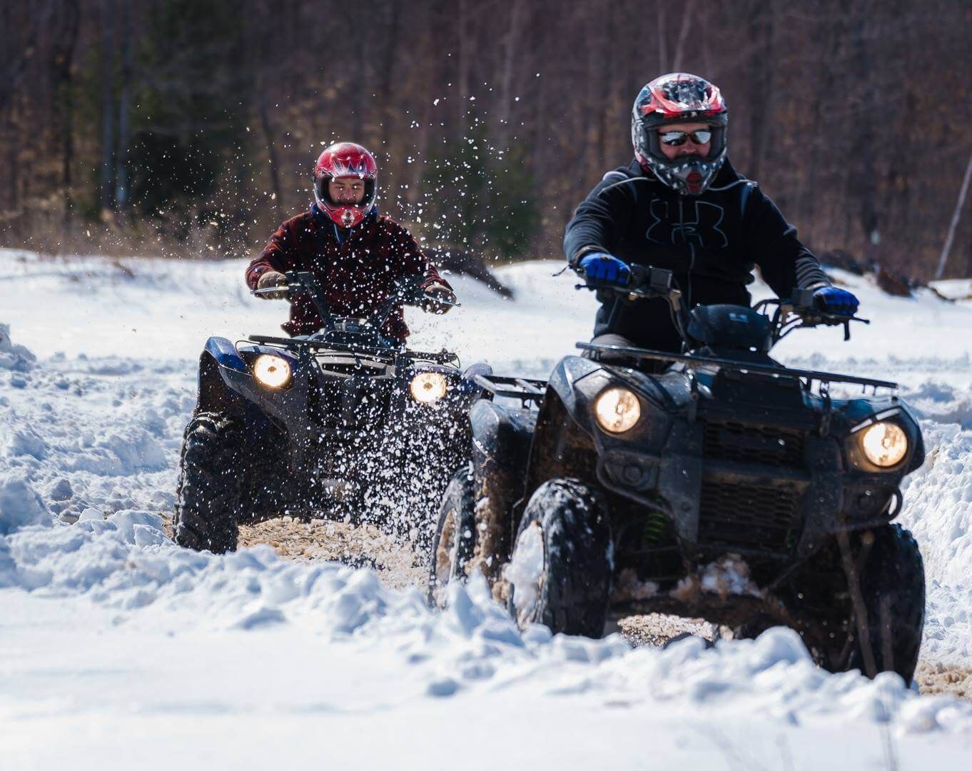 Two people are riding atvs in the snow.