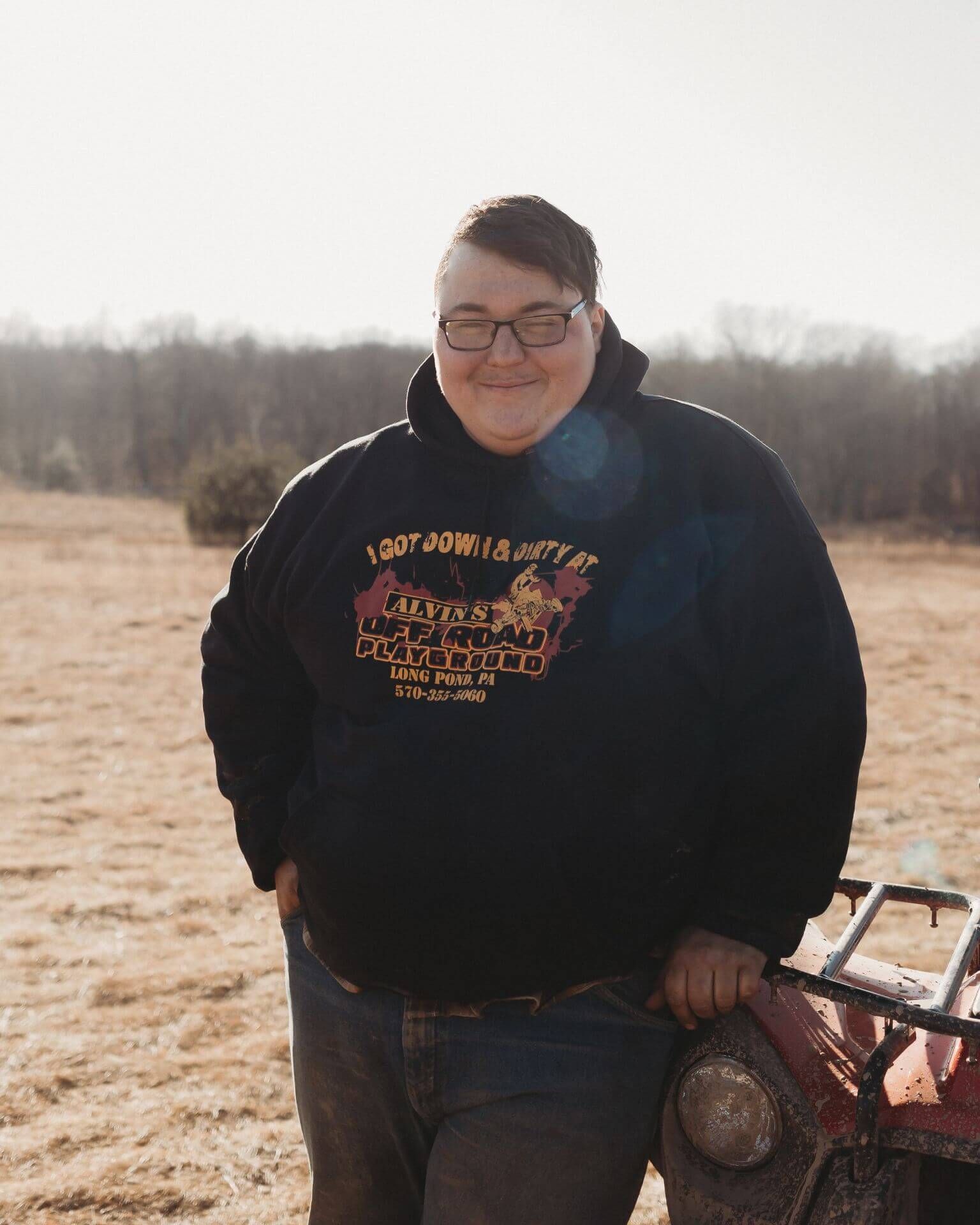 A man in a black hoodie is standing next to a red atv.