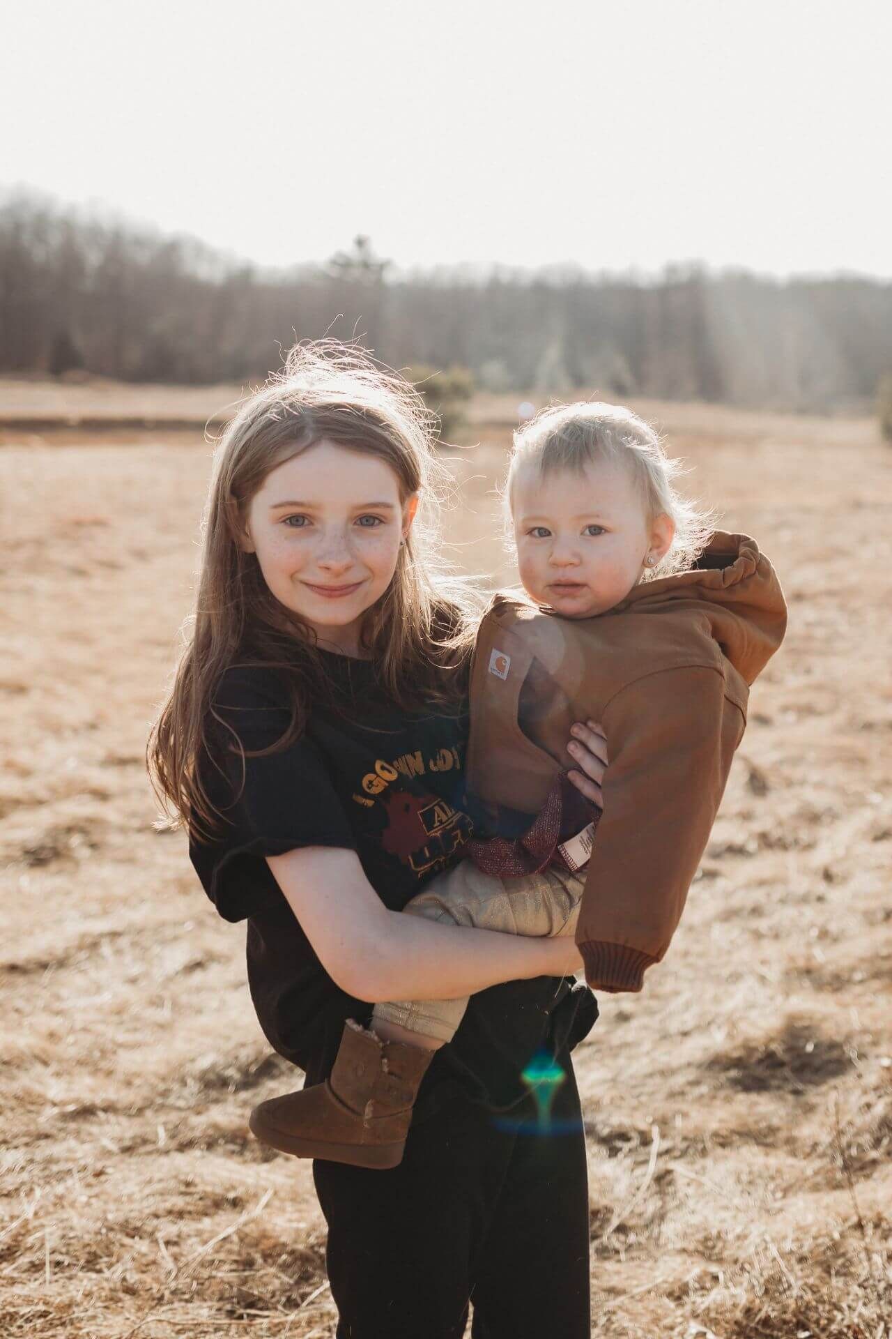 A girl is holding a baby in her arms in a field.