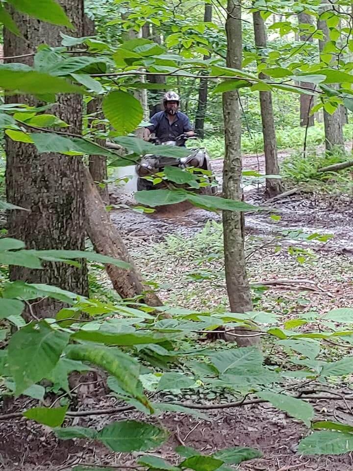 A man is riding a four wheeler through the woods.