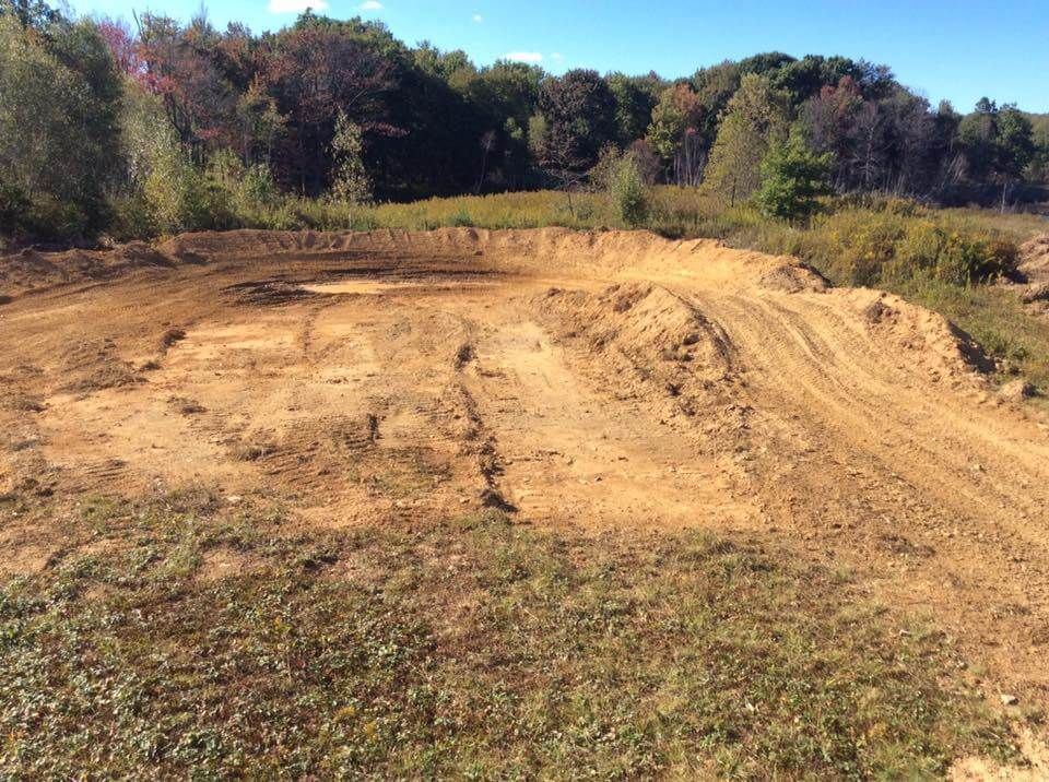 A dirt road going through a field with trees in the background.