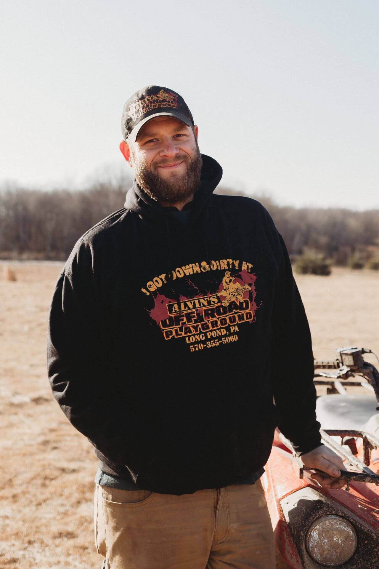 A man with a beard is standing next to a red atv in a field.