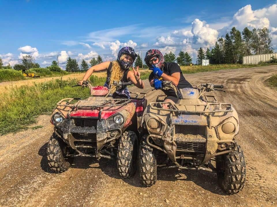 Two people are standing next to each other on atvs on a dirt road.