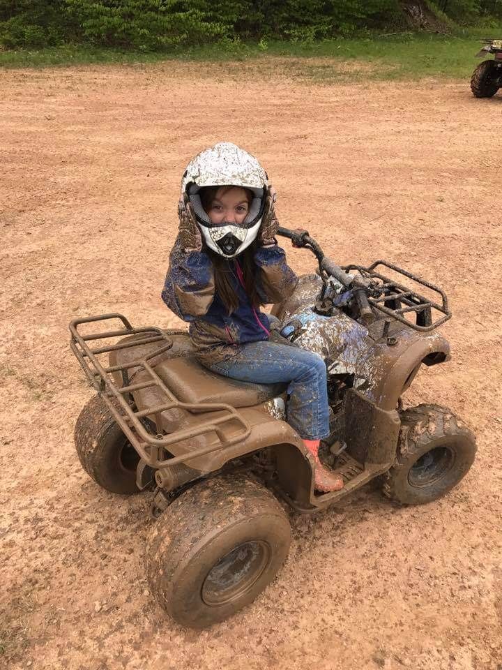 A young girl is riding a muddy atv on a dirt road.