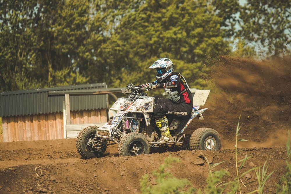 A man is riding a four wheeler on a dirt road.
