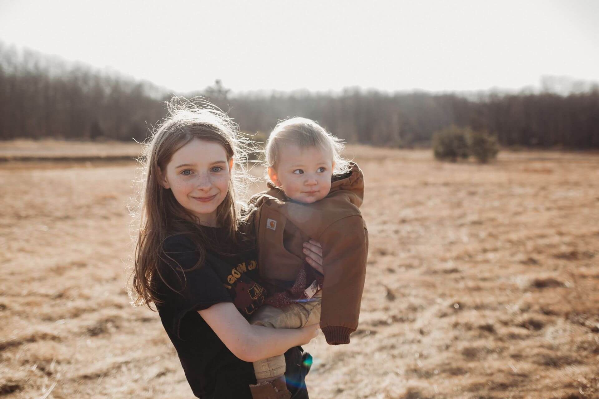 A young girl is holding a baby in a field.