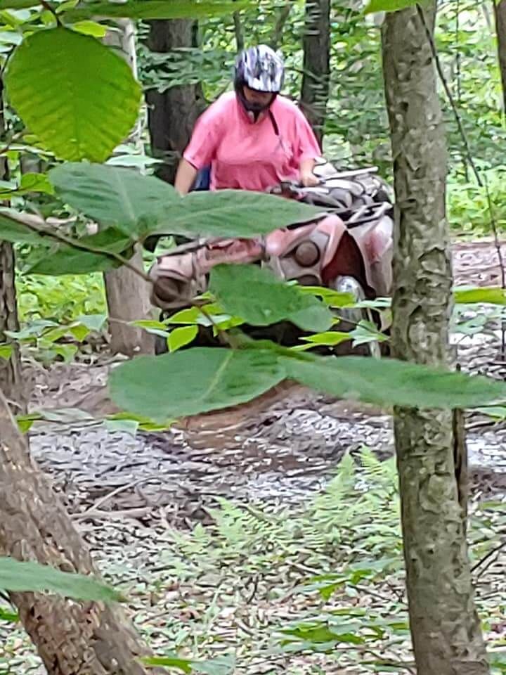 A woman is riding an atv through the woods.