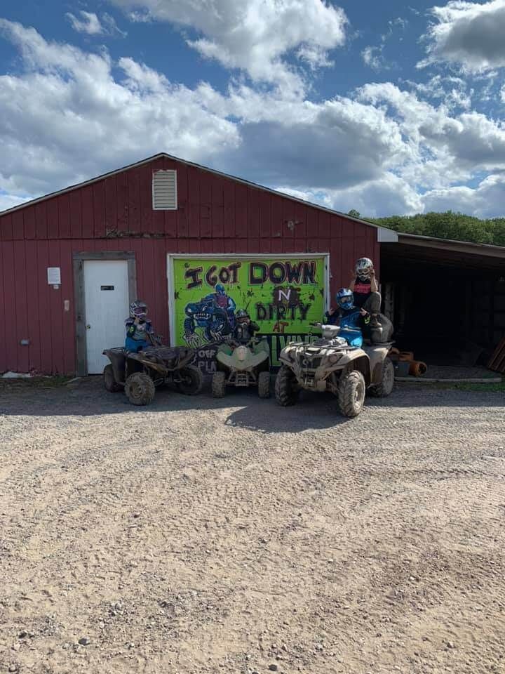 A group of people riding atvs in front of a red barn.