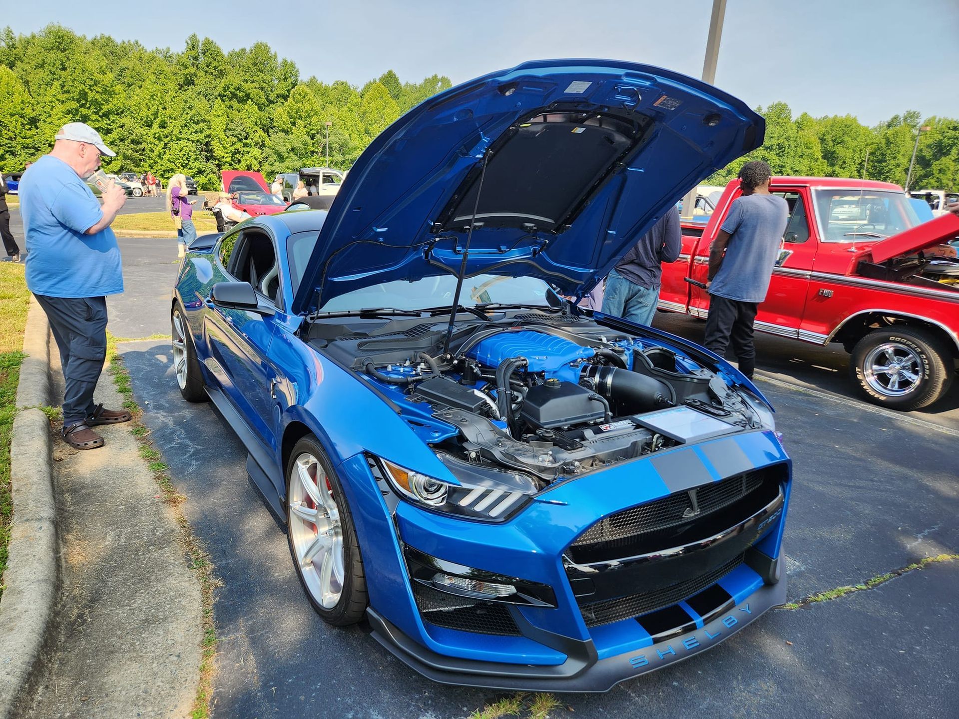 A blue car with the hood up is parked in a parking lot