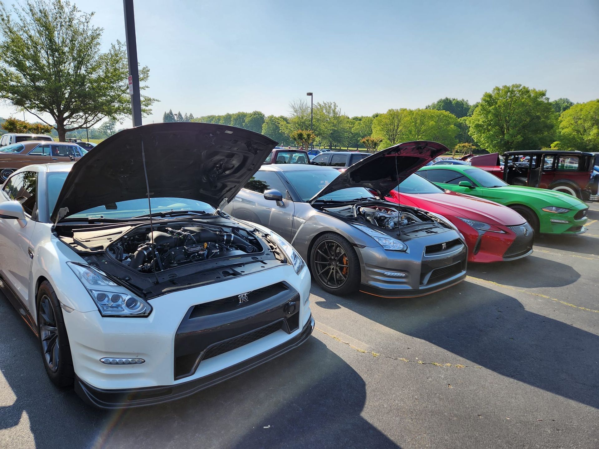 A row of cars with their hoods open in a parking lot