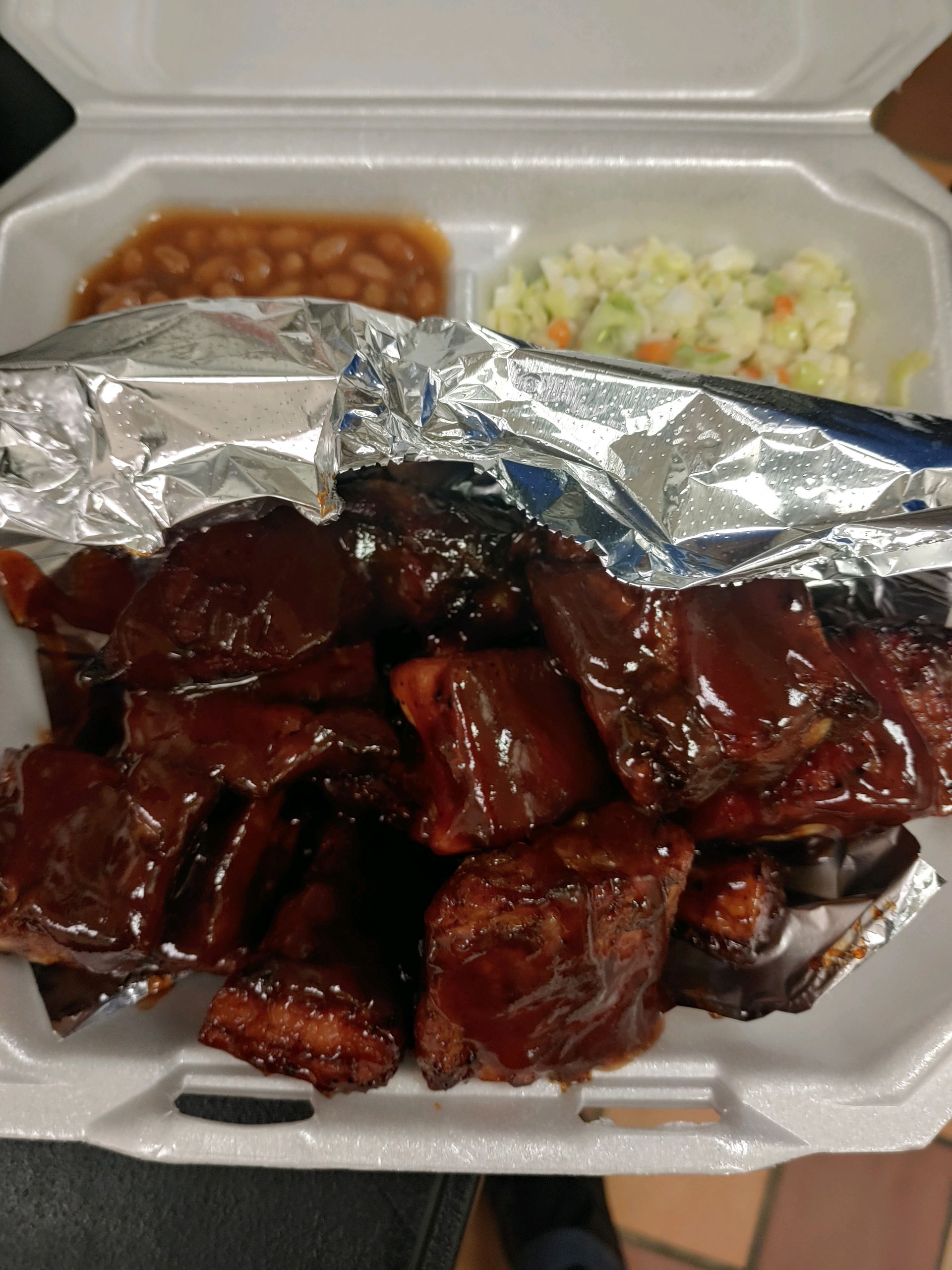 A styrofoam container filled with ribs beans and coleslaw