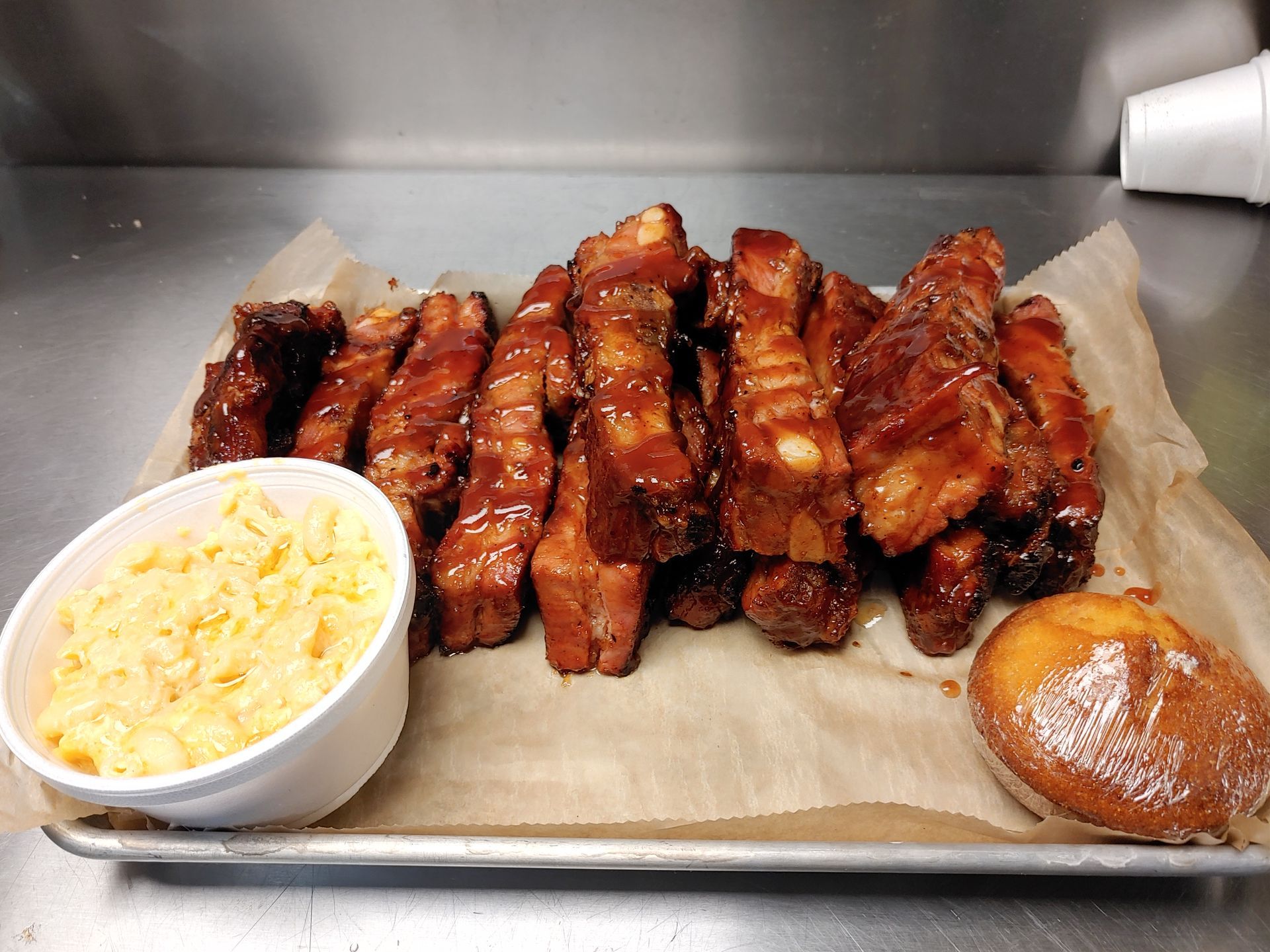 A tray of ribs with a bowl of macaroni and cheese and a donut.