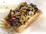 A sandwich with meat and vegetables is wrapped in plastic wrap