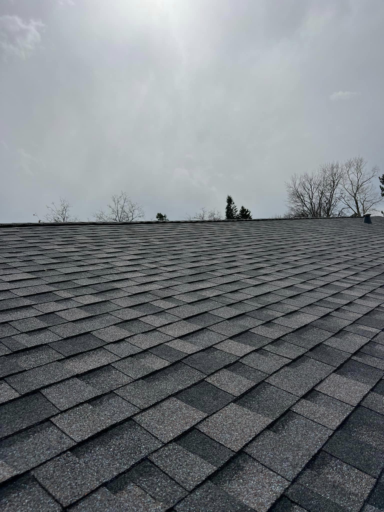 A black and white photo of a roof with a cloudy sky in the background.