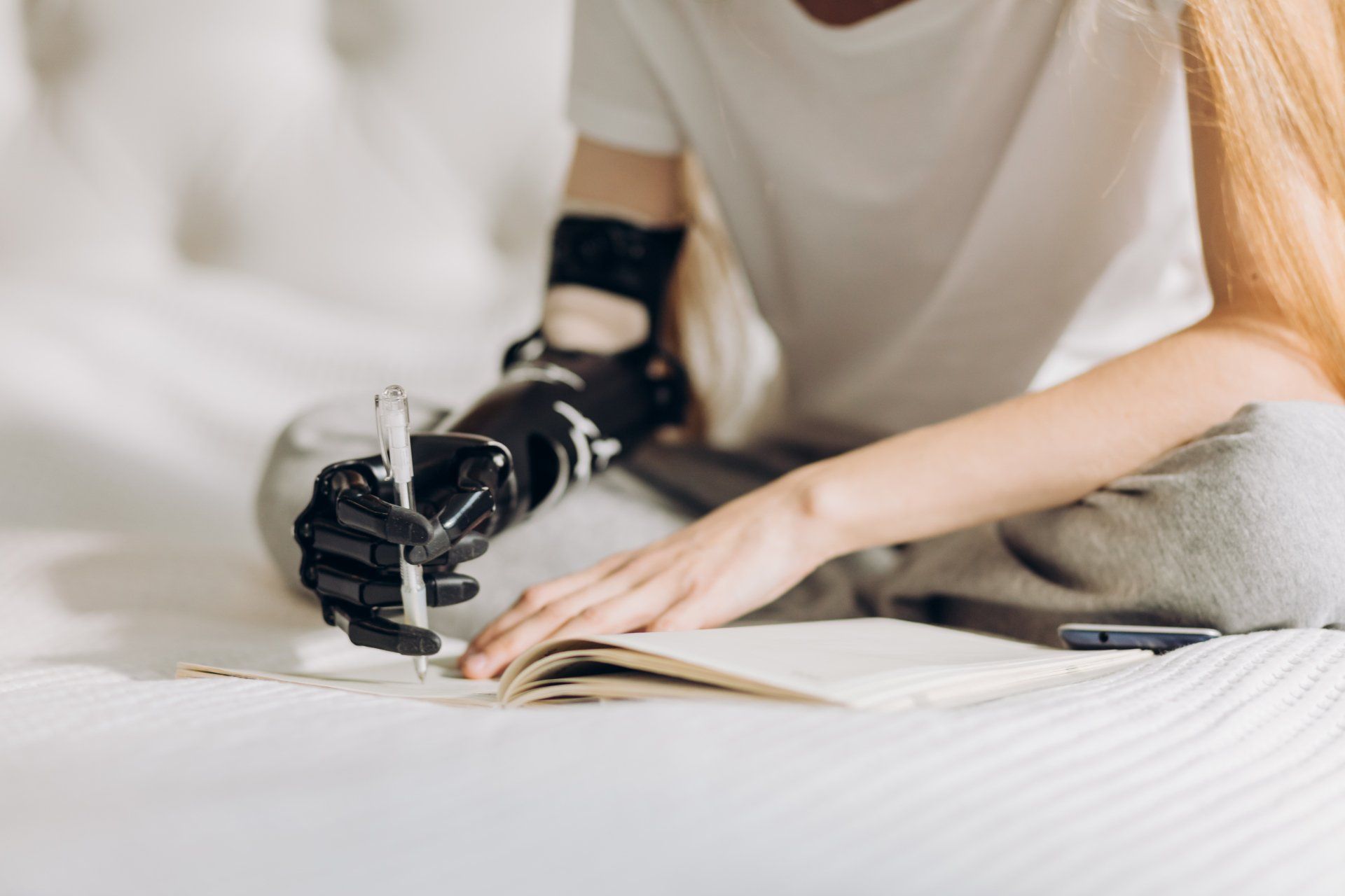 A woman with a prosthetic arm is writing in a notebook.
