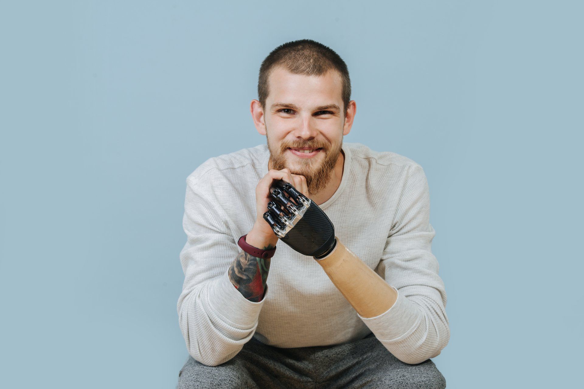 A man is sitting down with his hands folded and wearing gloves.