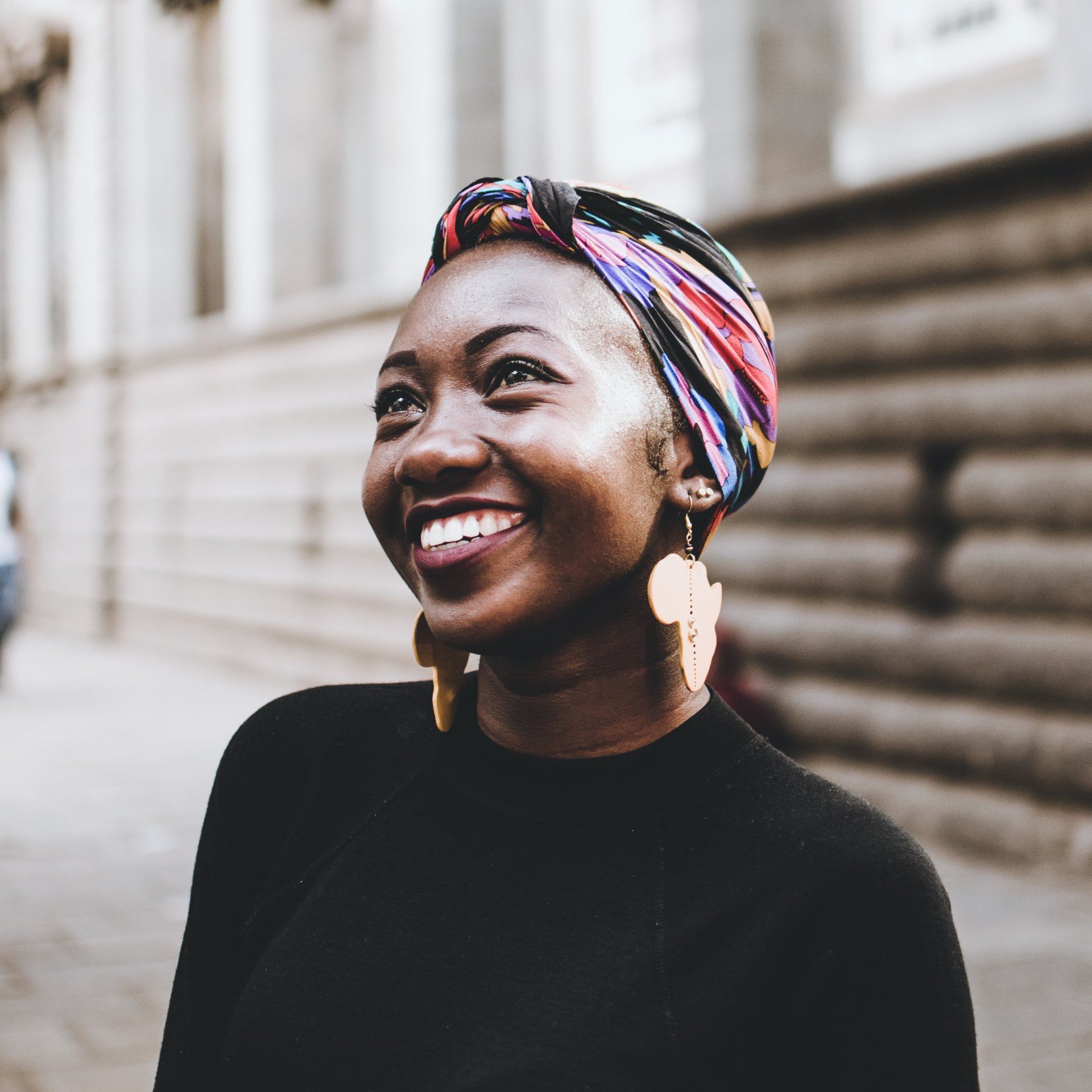 A woman wearing a head scarf and earrings is smiling