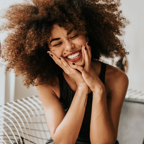 A woman with curly hair is smiling with her hands on her face