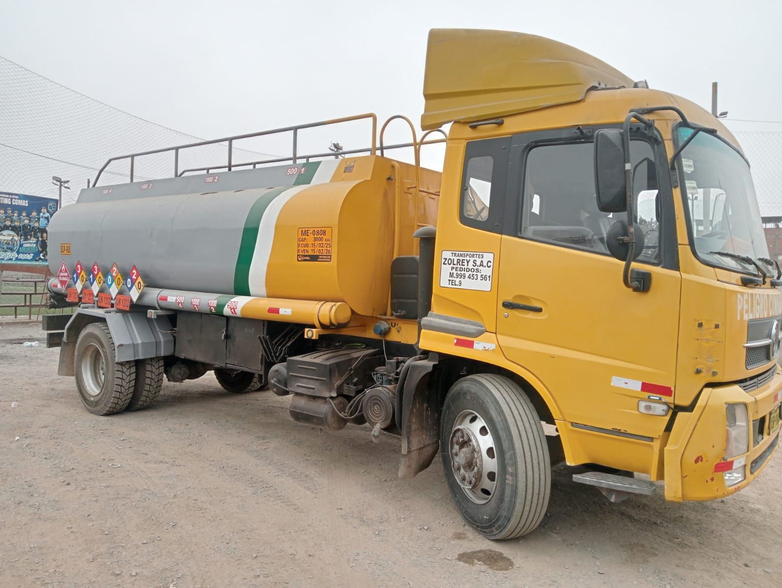 Un camión cisterna amarillo está estacionado en un lote de tierra.