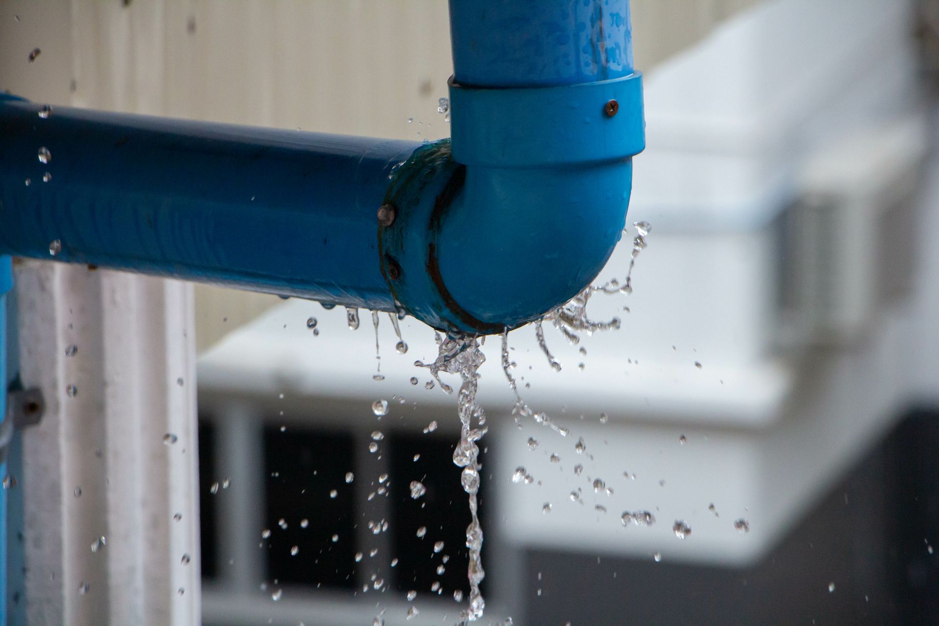 Closeup of a plastic pipe leaking water and creating splashes during a rainy day.