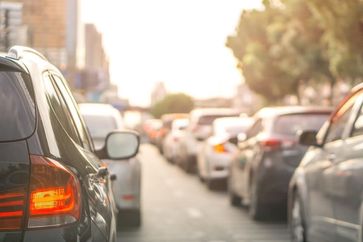 Traffic jam on a sunny city street, cars stopped, taillights glowing.
