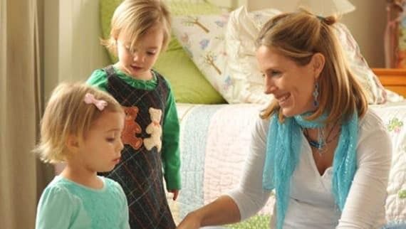 Woman kneeling with two young children, smiling.