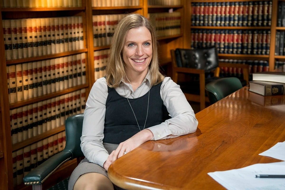 Woman in law office, smiling, seated at desk, bookshelves in background.