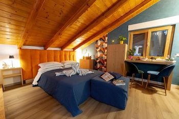 Accogliente camera da letto mansardata con soffitto in legno, letto matrimoniale, scrivania e nicchia con finestra in un'atmosfera calda.