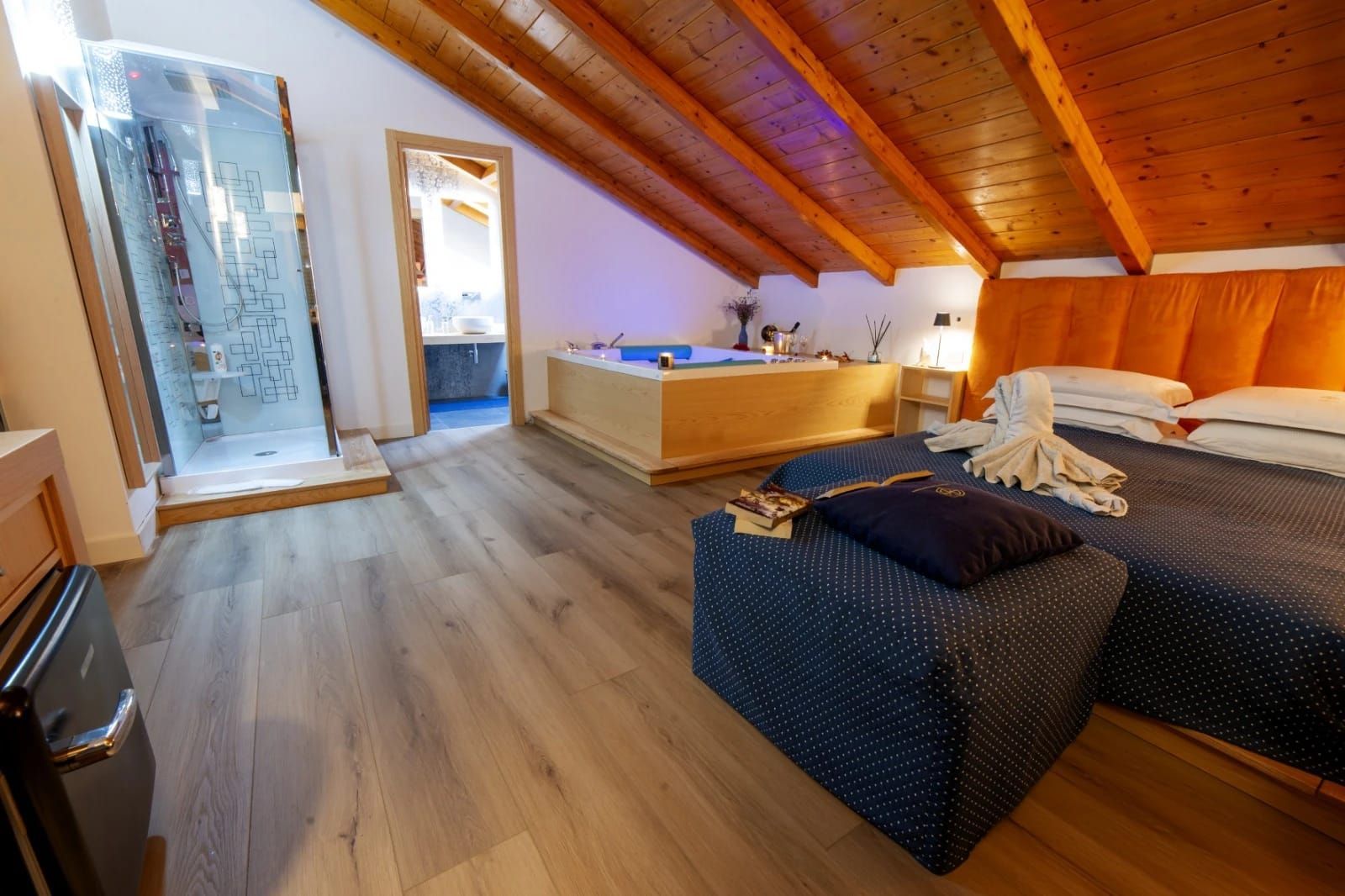 Accogliente camera da letto mansardata con soffitto in legno inclinato, due letti e una doccia in vetro nell'angolo.