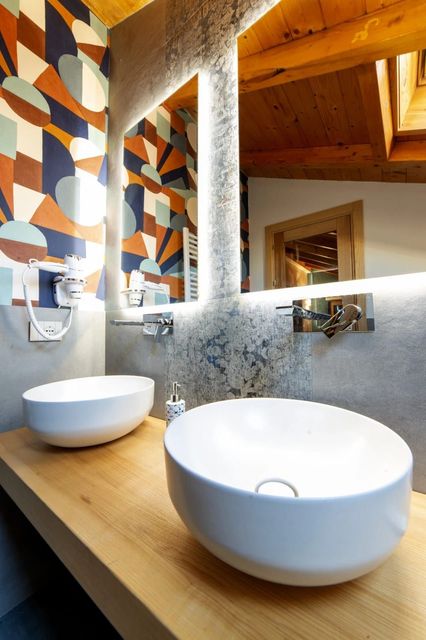 Bagno moderno con due lavabi a ciotola bianchi, piano d'appoggio in legno e specchio con motivo decorativo.