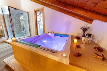 Bagno mansardato rivestito in legno con vasca idromassaggio angolare illuminata e candele sotto un soffitto inclinato