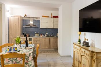 Luminosa cucina-sala da pranzo con mobili in legno, pavimento piastrellato, tavolo apparecchiato e TV a parete.