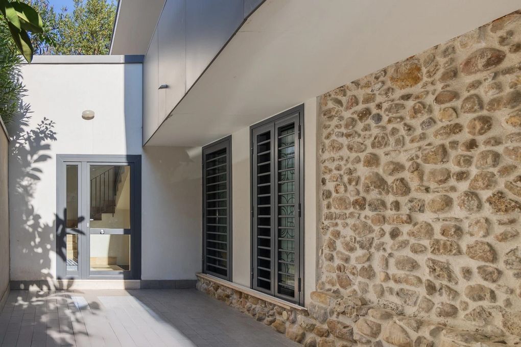 Esterno di una casa moderna con muro in pietra, facciata bianca e patio ombreggiato.