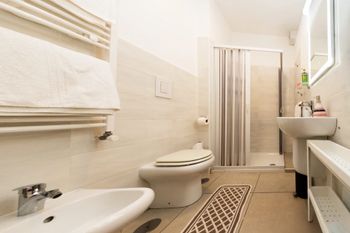 Bagno luminoso con bidet, WC, lavabo, doccia e portasciugamani.