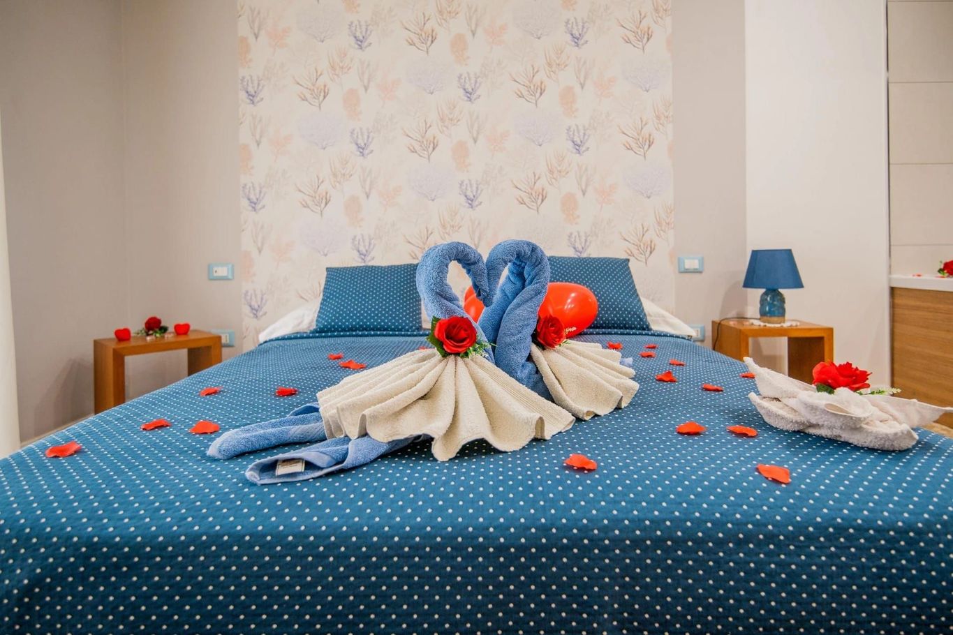 Letto blu decorato con cigni di asciugamani, petali di rosa e palloncini in una camera da letto