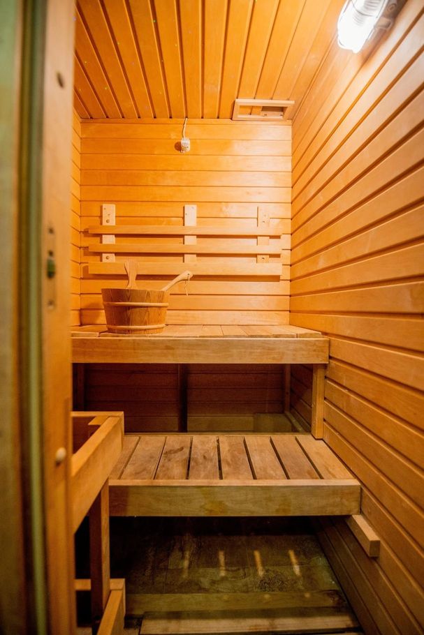 Sauna rivestita in legno con panche in legno e stufa, illuminata da una lampada a soffitto.