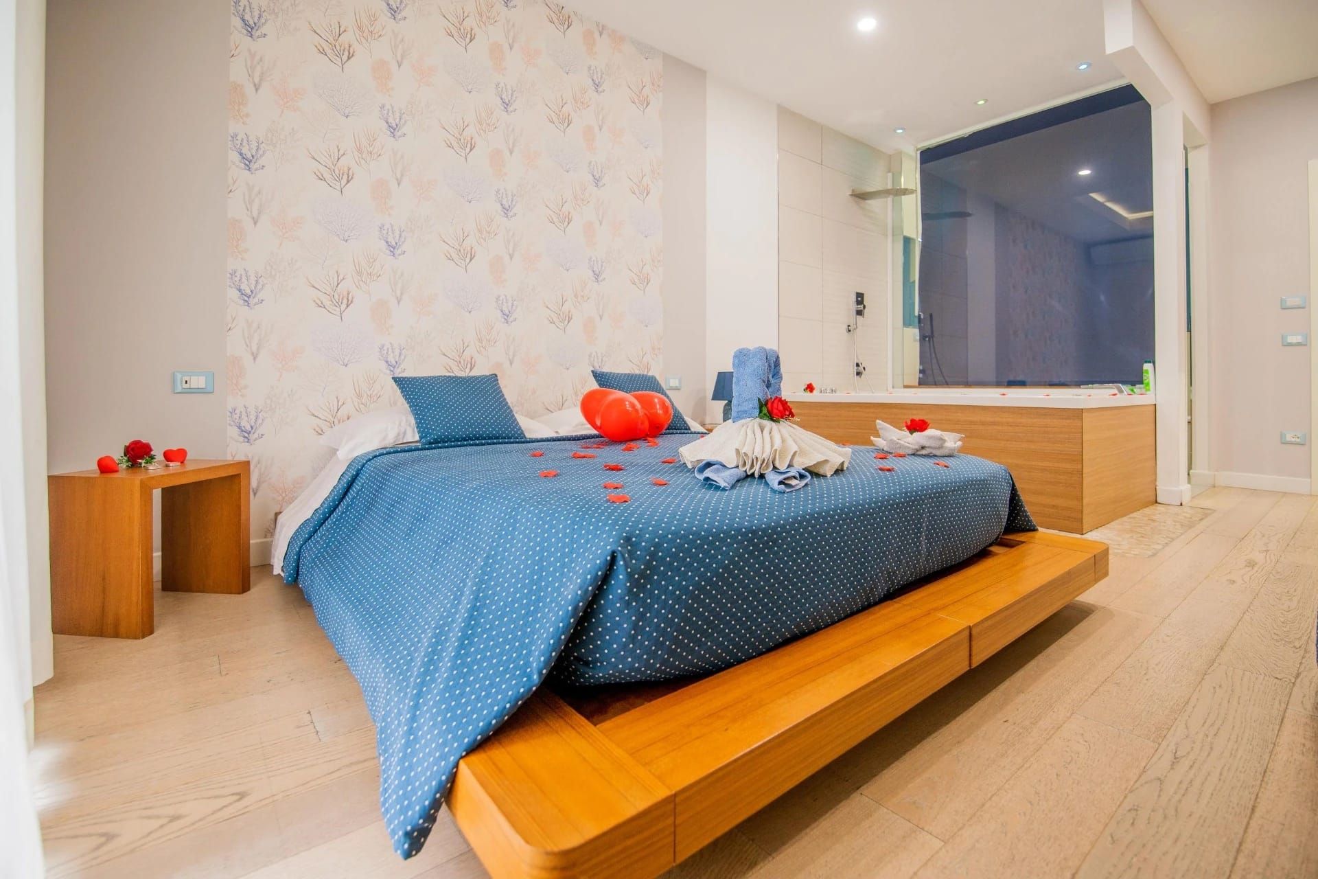 Camera da letto moderna con copriletto blu, letto a piattaforma in legno e grande finestra con vista notturna.