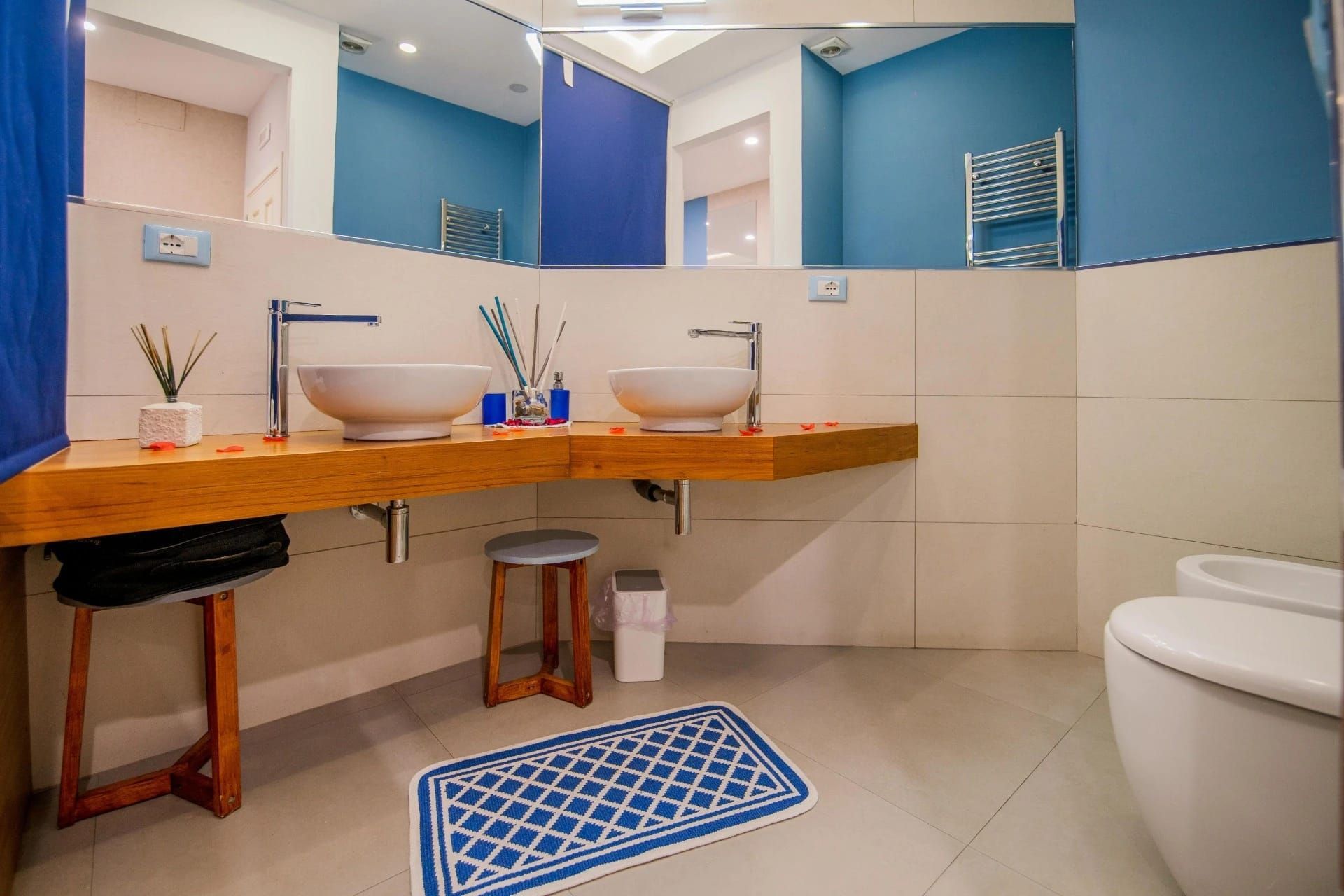 Bagno moderno con pareti blu, doppio lavabo, piano in legno, specchio e WC bianco.