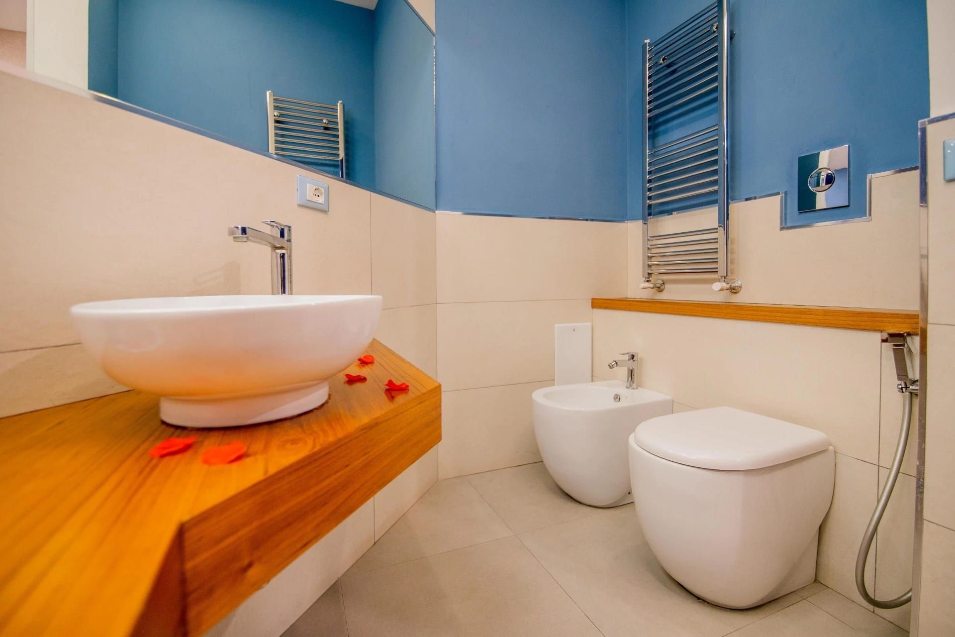 Bagno moderno con pareti blu, sanitari bianchi e piano lavabo in legno.
