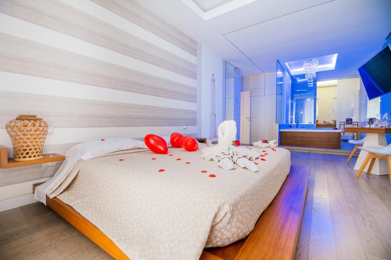 Camera da letto romantica con letto, palloncini a forma di cuore rossi e petali di rosa in un interno luminoso e moderno.