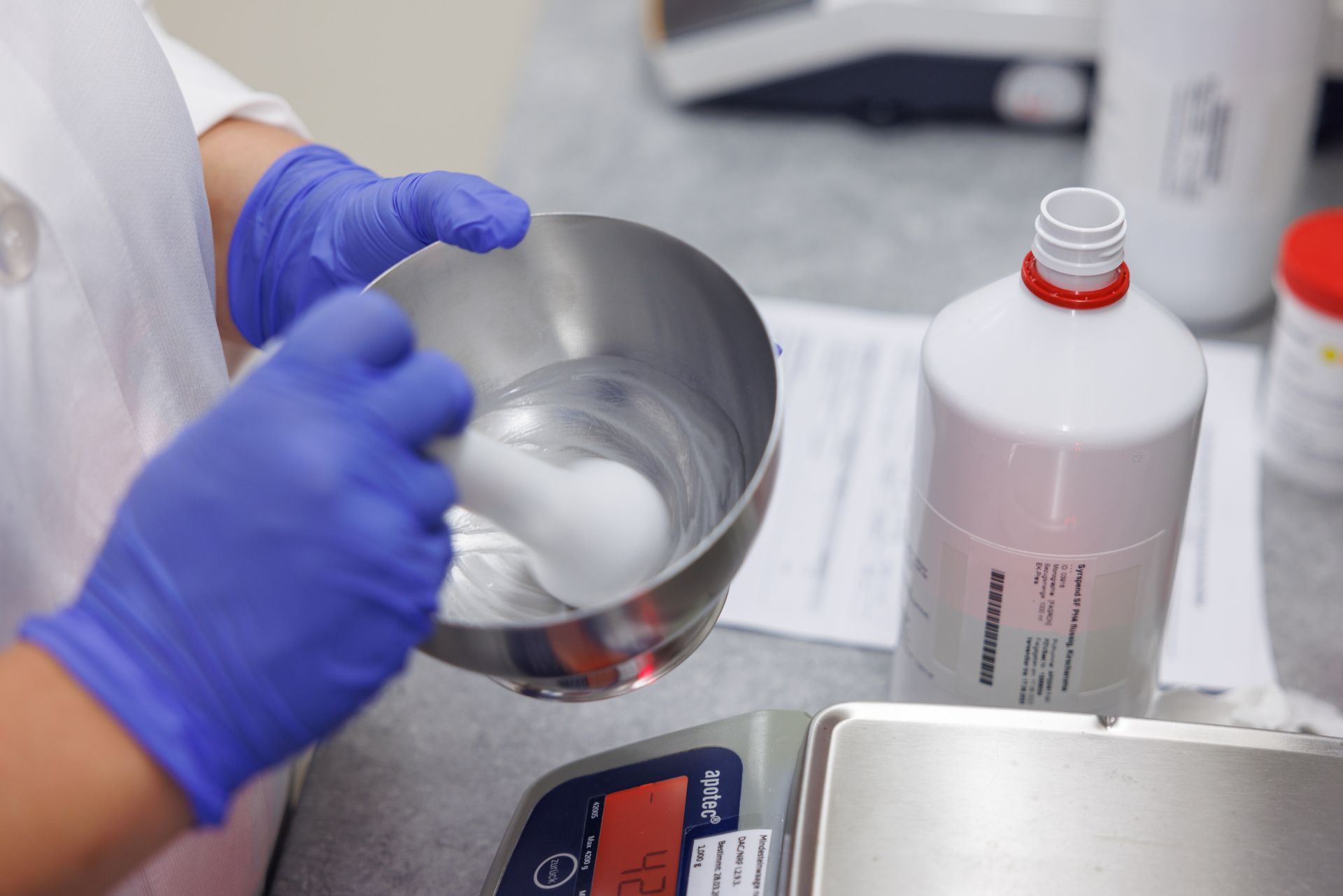 Eine Person mit blauen Handschuhen mischt eine Substanz in einer Schüssel.