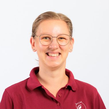 Eine Frau mit Brille und kastanienbraunem Hemd lächelt.