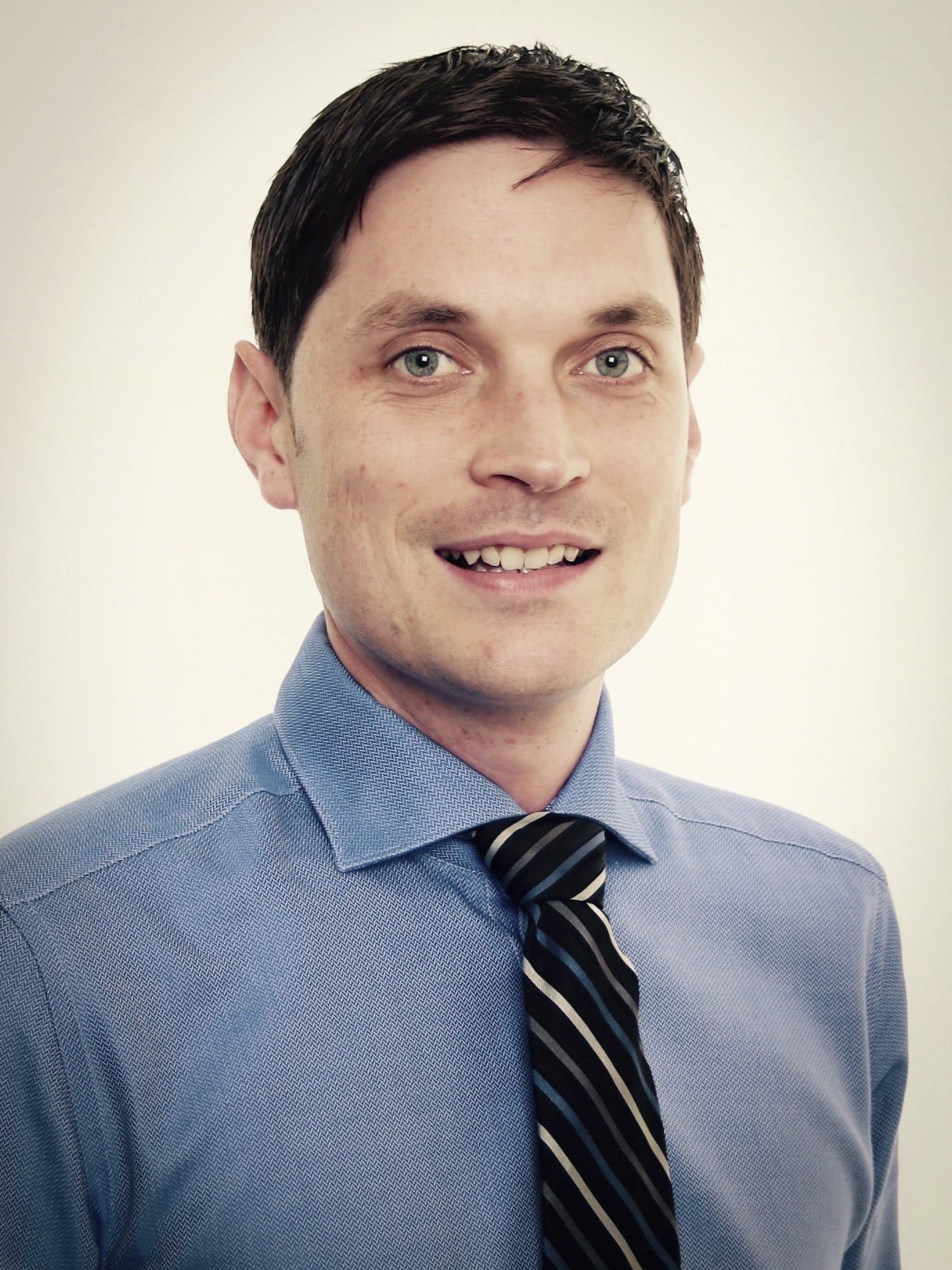 A man in a blue shirt and tie smiles for the camera