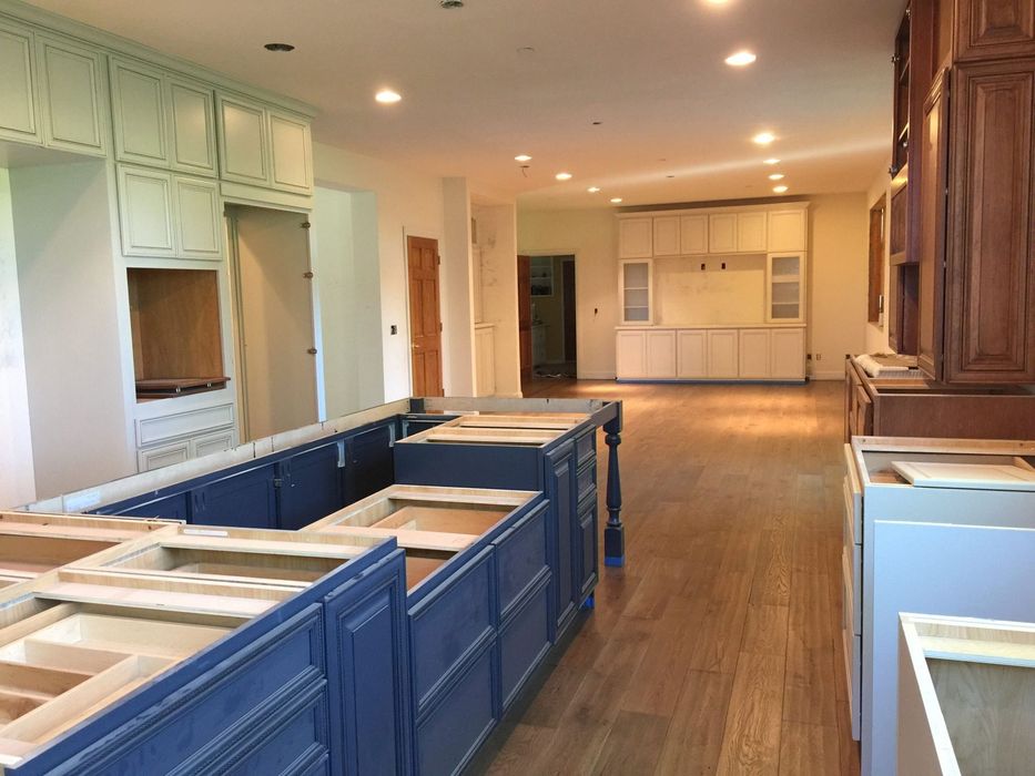 Interior view of a kitchen under renovation. Blue and white cabinets, hardwood floors, and recessed lighting are visible.